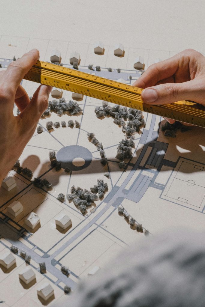 Close-up of hands measuring an architectural model with a ruler under natural light.